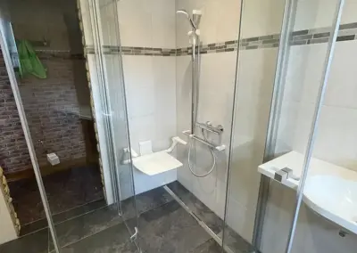 Gommern: Anordnung einer ebenerdigen Dusche. Hier insbesondere Hilfsmittel wie Duschklappsitz mit Armlehnen, Haltegriff mit verschiebbarer Brausehaltestange und Thermostatmischbatterie.